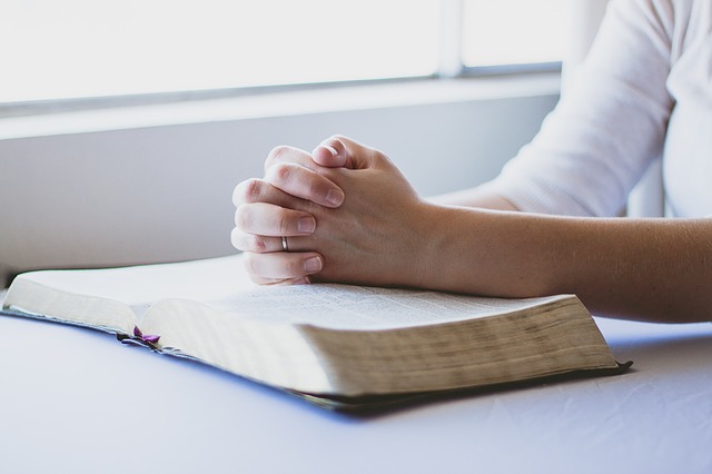 Hands praying with a bible over a table. Concept, meditating on God’s Word.