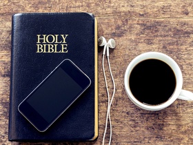 Mobile device on the Holy Bible next to a black coffee cup sitting on a wooden background, vintage color.