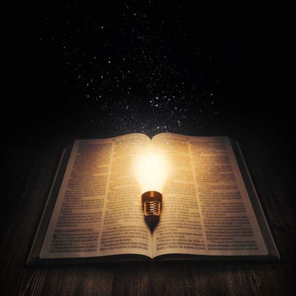 A light bulb lighting up an open bible in the dark on a wooden table. Bibles That Are Easy to Read, concept.