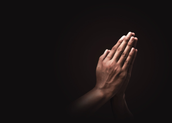 A pair of hands demonstrating a prayerful pose on a dark backdrop, conveying faith in religion and reliance on God. A representation of optimism or affection and reverence.