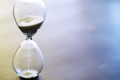 A picture of sand running through the bulbs of an hourglass, showing how much time remains before a deadline, on a dark floor with text space.