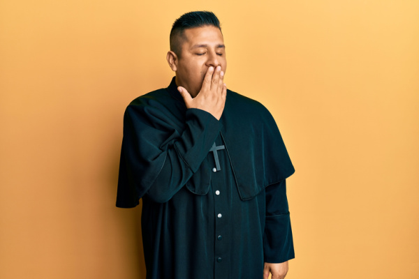 On a yellow backdrop, a young religious figure is seen yawning tiredly with his hand covering his mouth. He appears to be restless and tired.