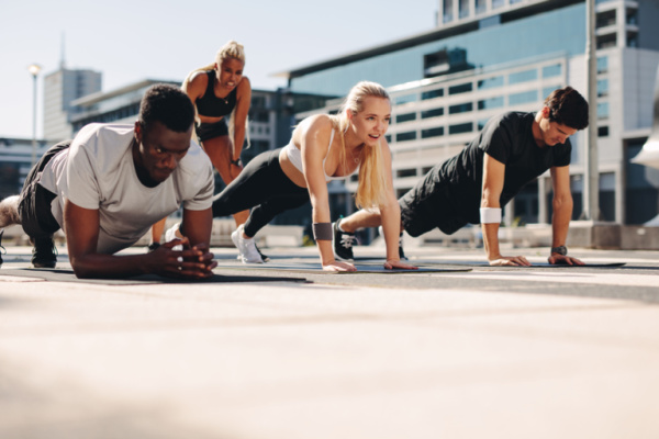 A group performing core-strengthening exercises outside on an exercise mat. A group of athletes exercising together in an urban setting.