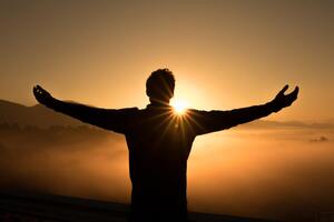 A person stretching out his arms toward the sun on the mountain peaks. Concept what is Spiritual Awakening in Christianity.