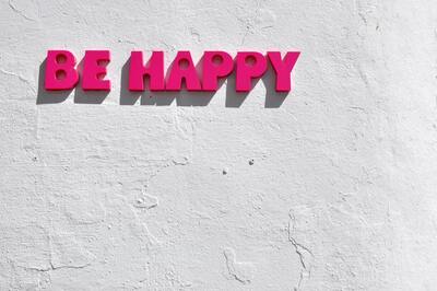 A concrete background with a sign written in pink text that says "Be Happy."