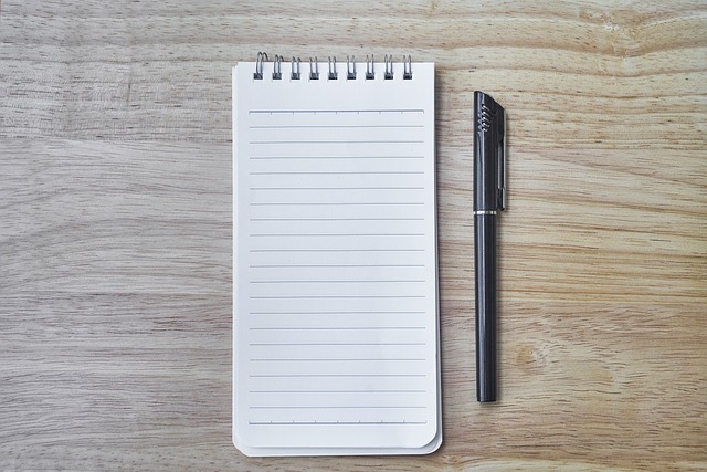 A notepad and pen are sitting on a wooden desk. Note-taking is a method of concentrating on God's Word.