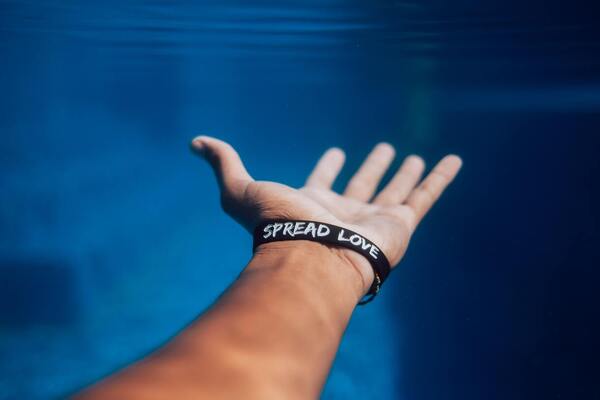 A person with an outstretched arm wearing a "Spread Love" bracelet.