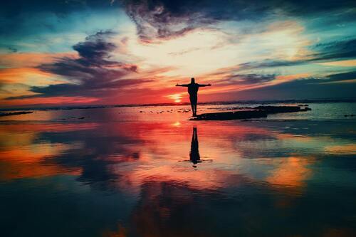 A person is standing on a rock with their arms wide open in a body of water. Concept of how to deal with stress spiritually.