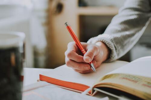 A person writing in a journal using a red pen.