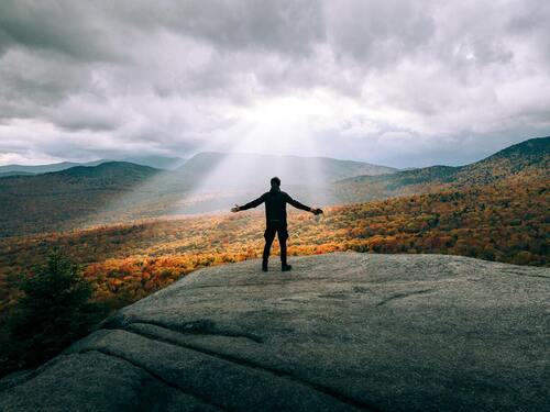 An individual standing on a large rock, gazing at the colorful autumn leaves.