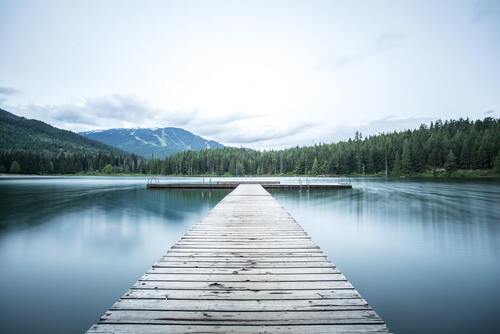 During the daytime, a sea dock is made of gray wood situated amidst green pine trees and a white sky—a concept of a personal relationship with Jesus.