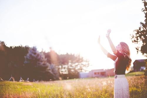 A woman holds up her hands in front of green meadows.