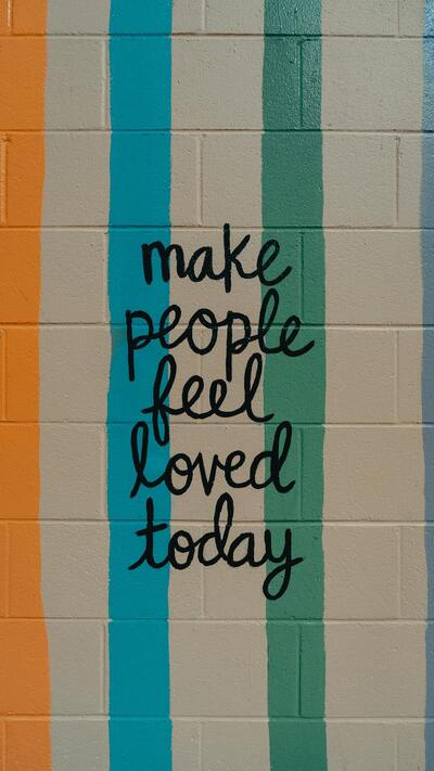 The phrase "Make people feel loved" is written on a wall of colored bricks.