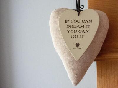 A wooden heart shape attached to a plush heart shape gray background decorated with the phrase 'If you can dream it, you can do it.' Concept, spreading positivity.