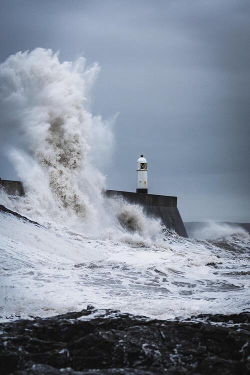 During the daytime, large waves forcefully collide with a lighthouse—concept, calmness in the storm.