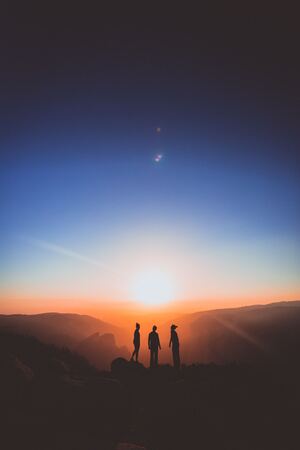 Three figures stand on a mountain range with their backs toward the viewer, looking at the sunrise. Concept, God uses imperfect people.