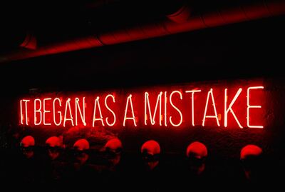 A brightly lit neon sign displaying the wording 'It began as a mistake.’