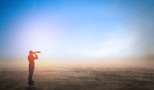 A businessperson gazes into the distance through binoculars against a sunset sky, envisioning the future—the concept of fulfilling your purpose.